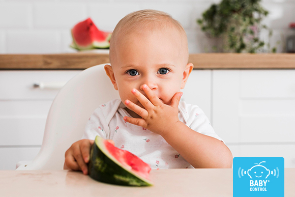 Bebé comiendo sandía en una trona durante la alimentación complementaria para favorecer la salud bucodental