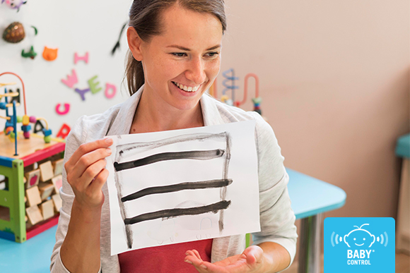 Profesora de escuela infantil sonriente mostrando un dibujo infantil, reflejo del cuidado del equipo educativo durante el segundo trimestre