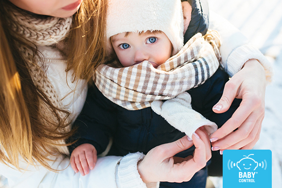 Bebé recién nacido con gorro y abrigo en brazos de su mamá, protegido del frío invernal y mostrando cuidados para mantener su temperatura estable.