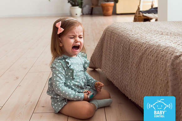 Niña pequeña llorando en el suelo de la habitación de sus padres durante una rabieta infantil