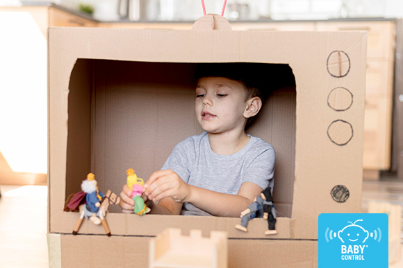 Niño jugando al juego simbólico con una televisión de cartón y personajes de papel para representar una película, desarrollando su creatividad e imaginación.